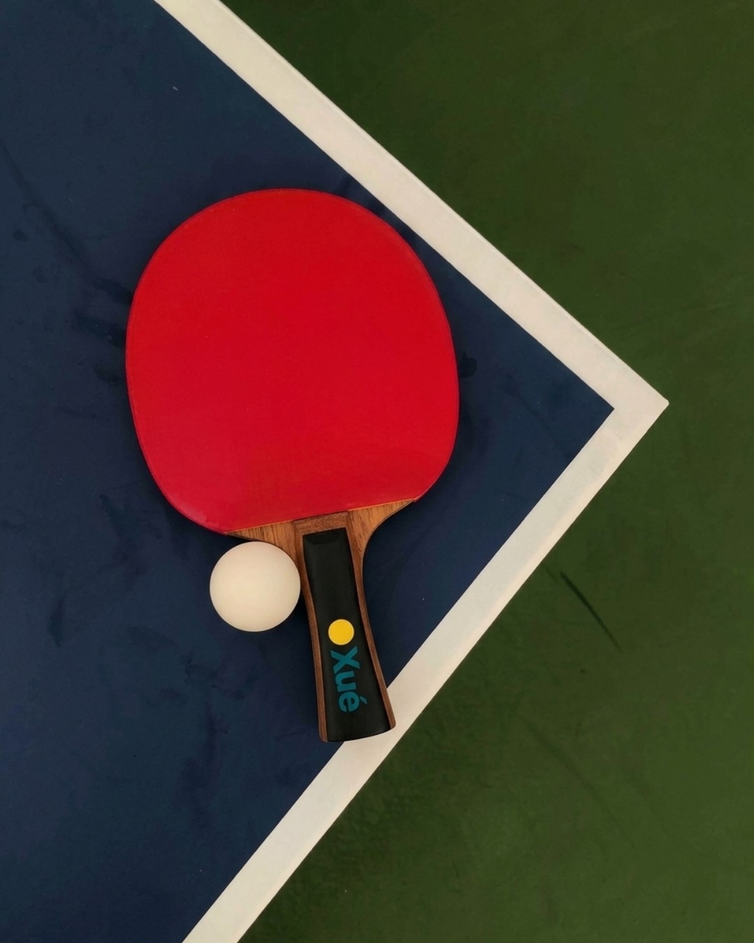 Raqueta roja y pelota blanca sobre la esquina de una mesa de tenis de mesa