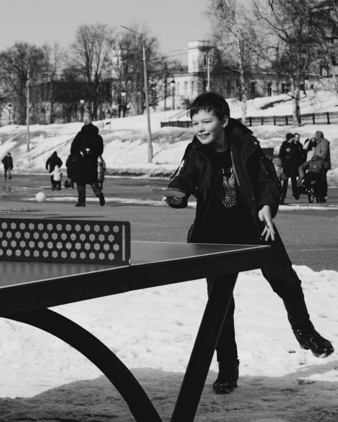 Niño sonriente jugando tenis de mesa al aire libre en un parque nevado